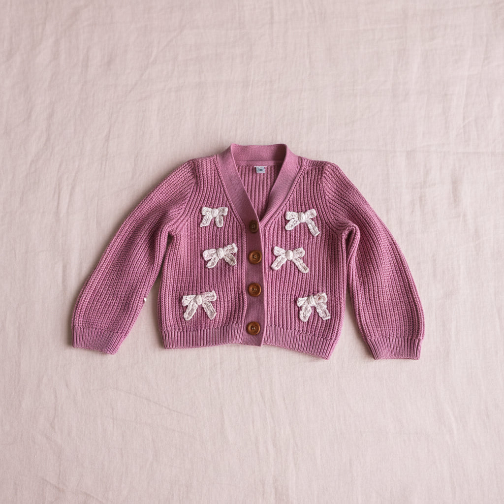 Pink cardigan with bow details on a pink background