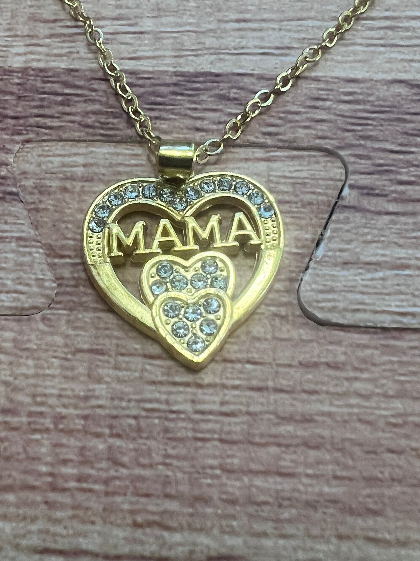 Gold necklace with 'MAMA' heart pendant on a wooden surface