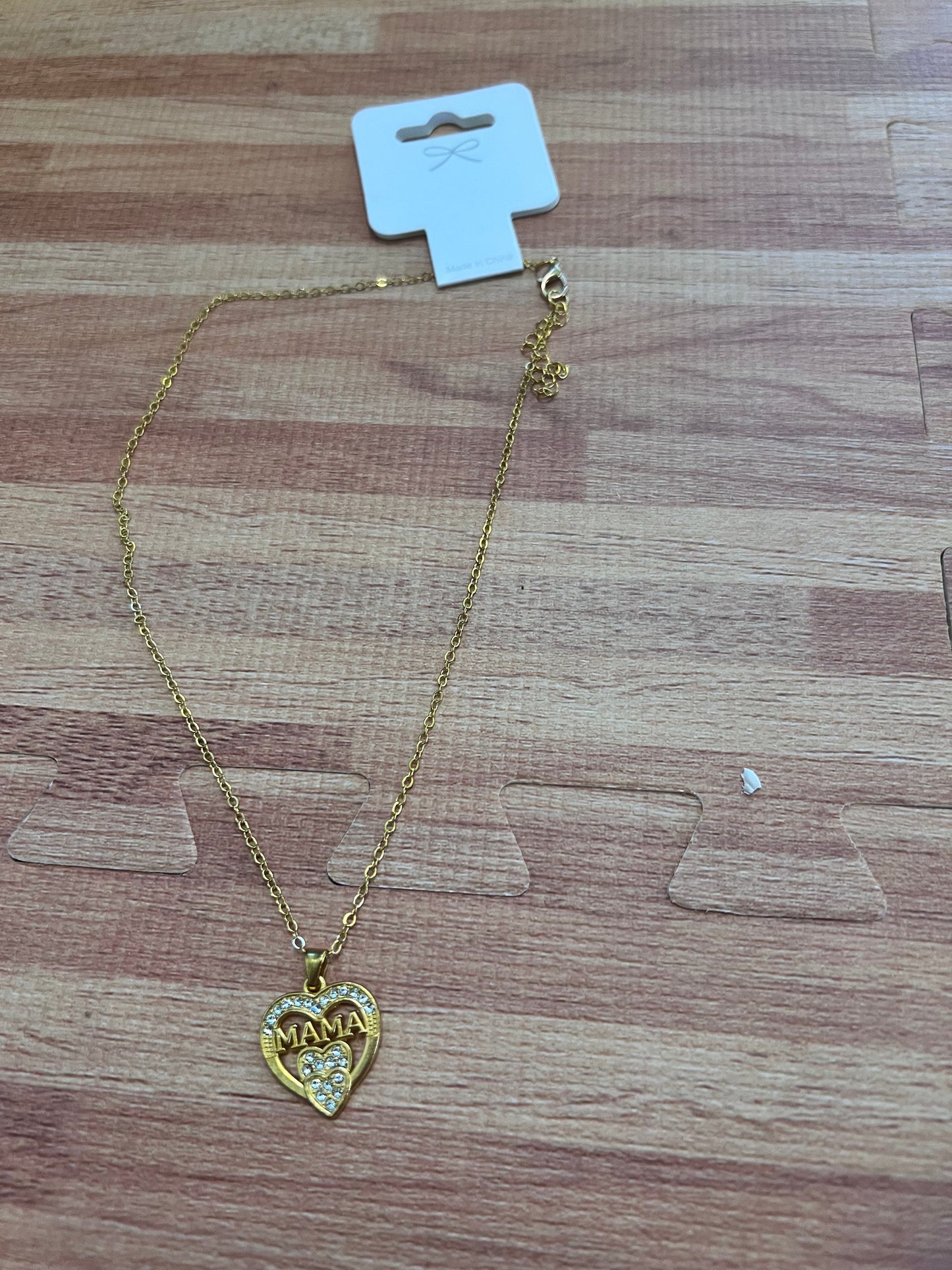 Gold necklace with a heart-shaped 'MAMA' pendant on a wooden surface