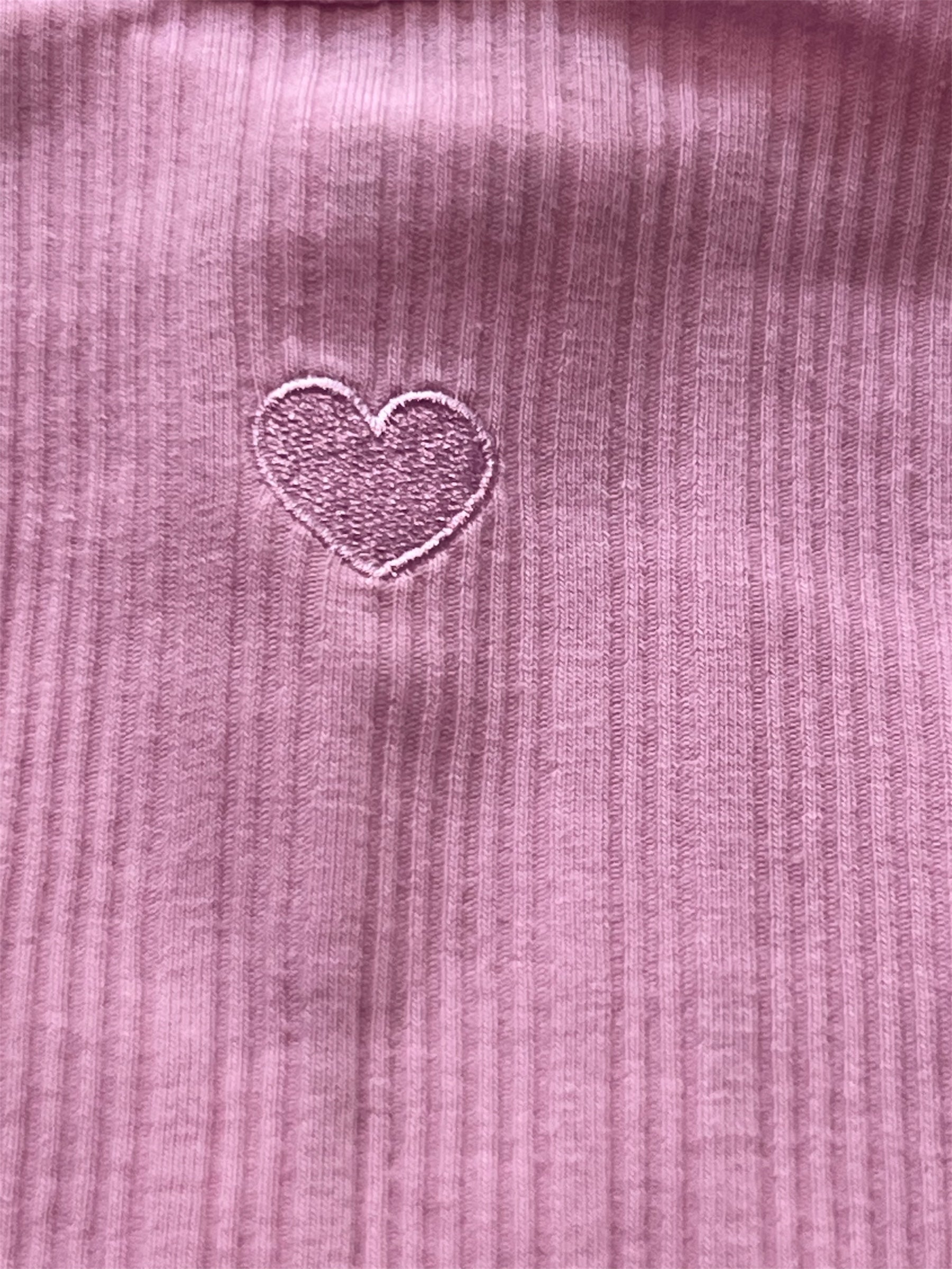 Close-up of a pink textured fabric with a heart-shaped embroidered design.