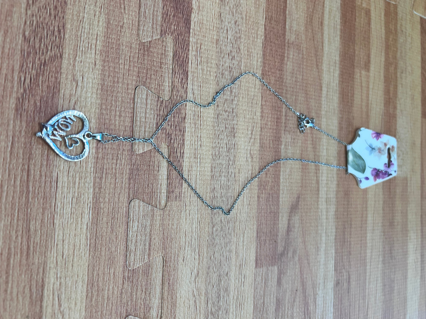 Necklace with heart-shaped clasp and floral pendant on a wooden surface