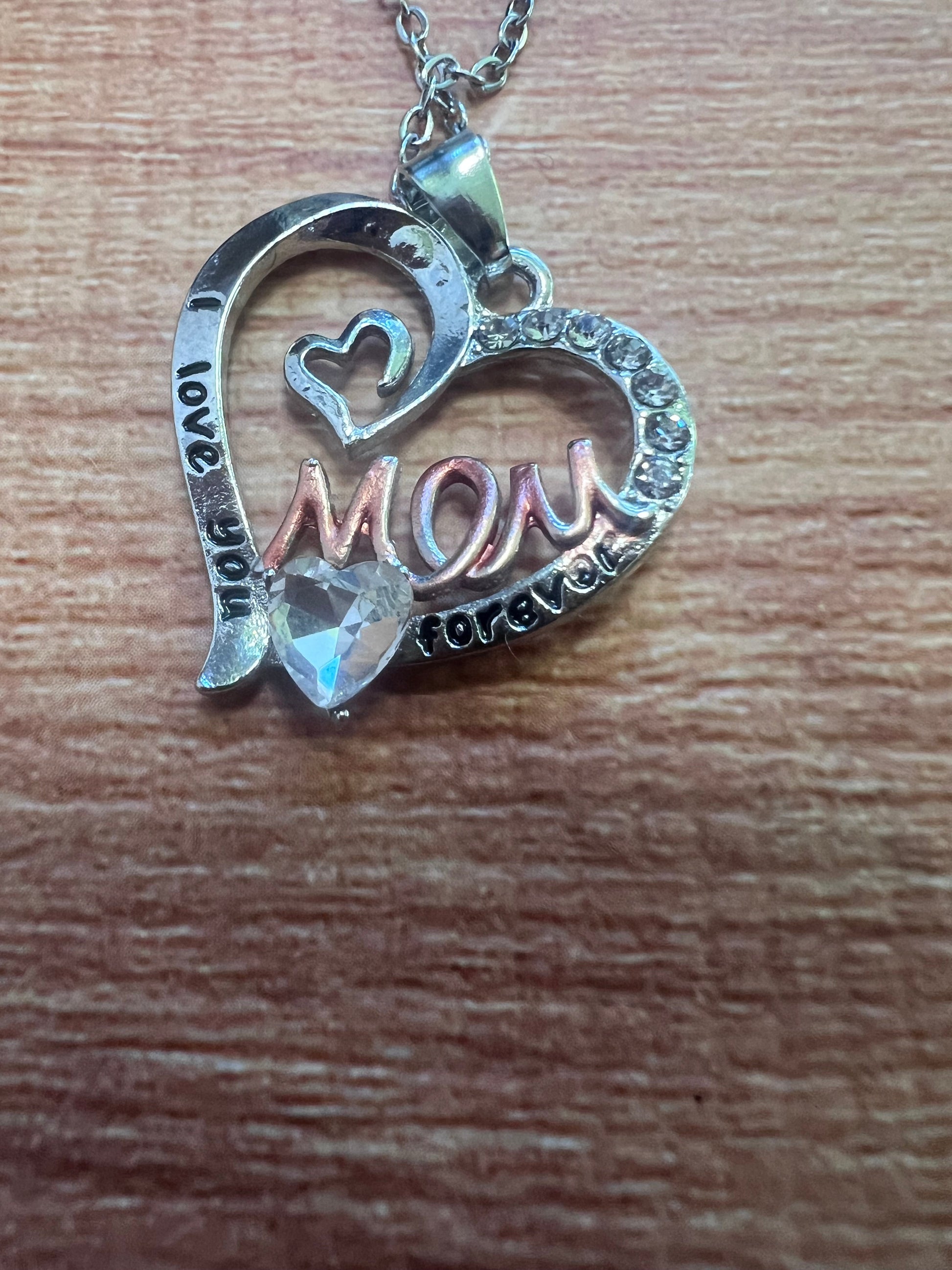 Heart-shaped silver pendant with 'I love you mom' text on a wooden surface